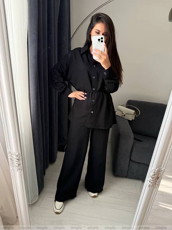 Person wearing a black outfit taking a mirror selfie in a room with a gray sofa.