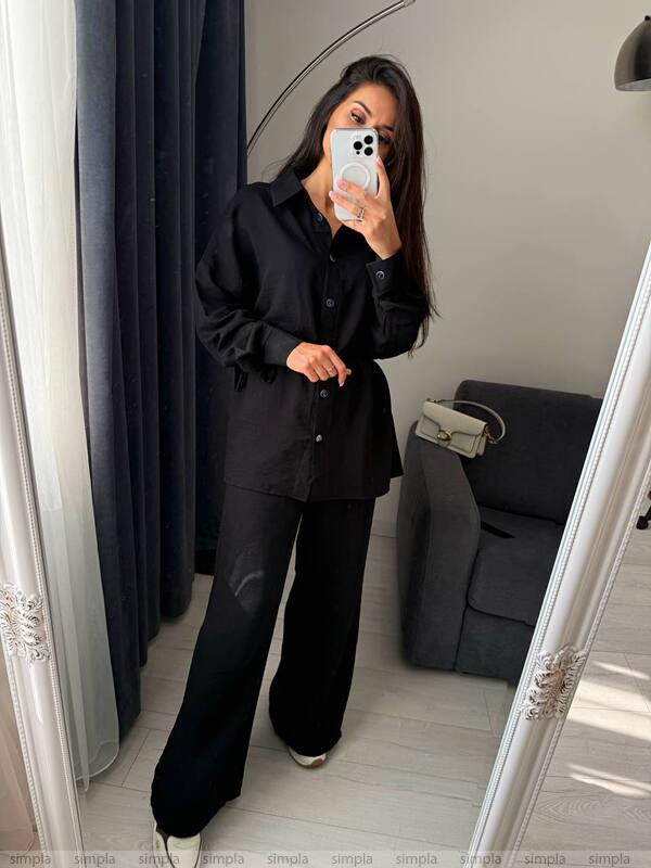 Person taking a mirror selfie wearing a black outfit in a room with a gray sofa.