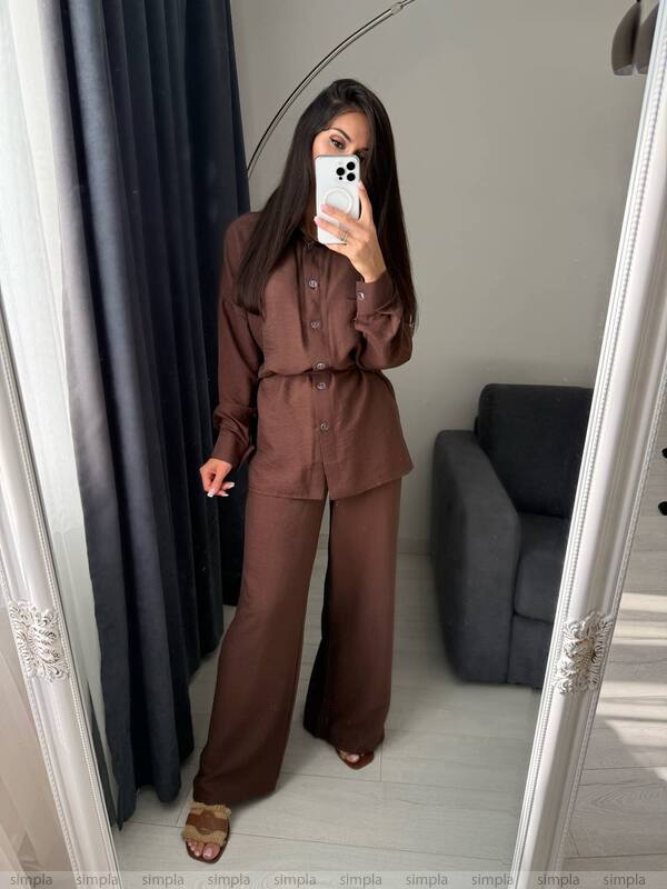 Person wearing a brown outfit taking a mirror selfie in a room with a gray sofa.