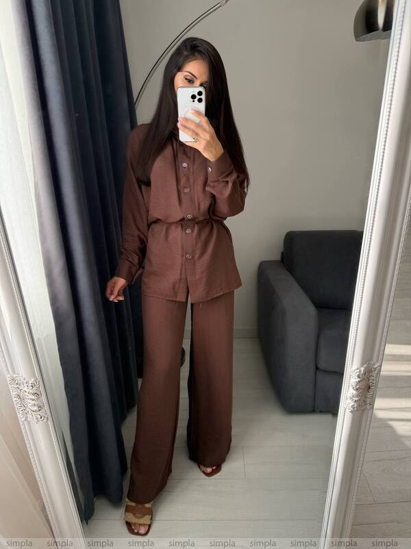 Person wearing a brown outfit taking a mirror selfie in a room with a gray sofa.