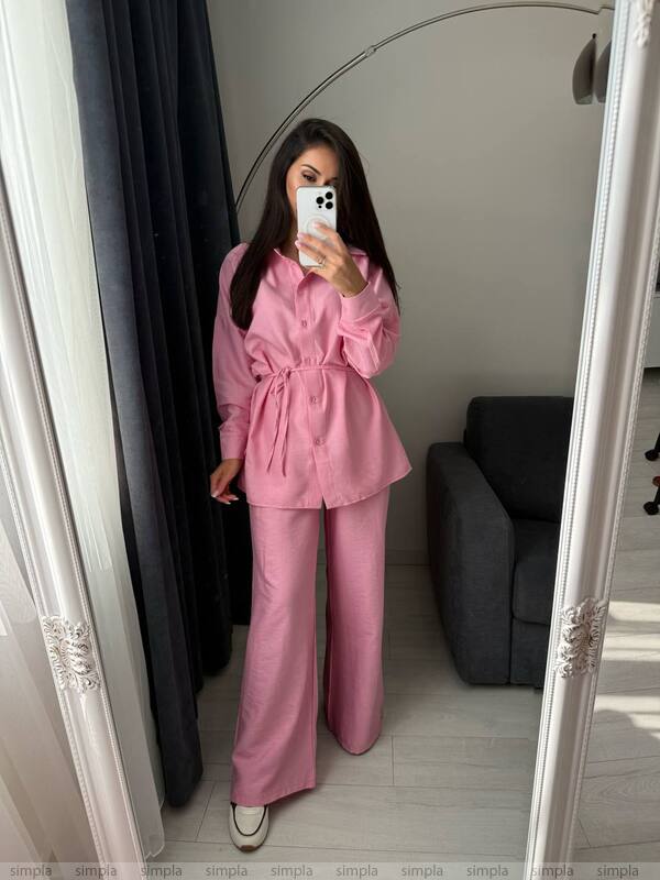 Person wearing a pink outfit taking a mirror selfie in a room with a gray couch.