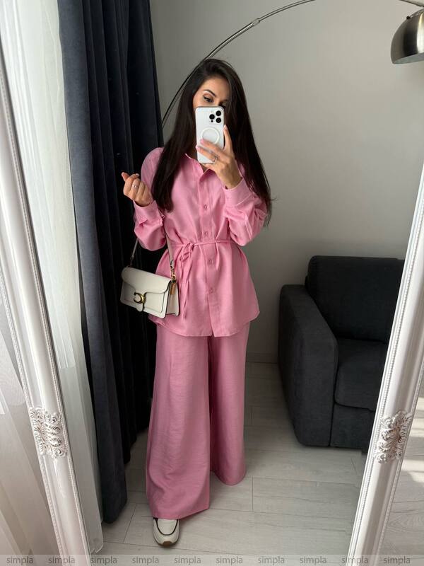 Woman taking a mirror selfie wearing a pink outfit in a room with a gray sofa.