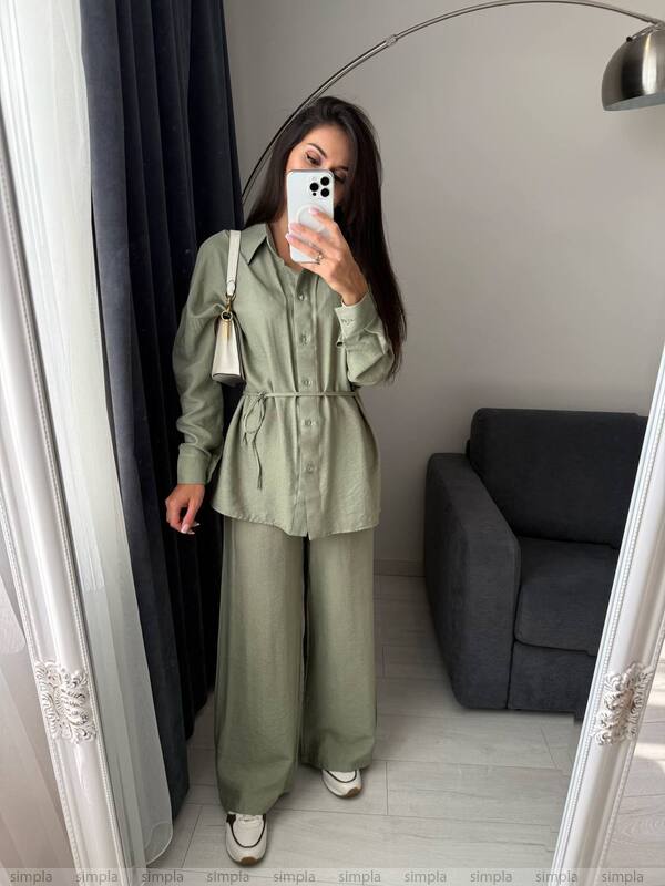 Person wearing a green outfit taking a mirror selfie in a room with a gray sofa.