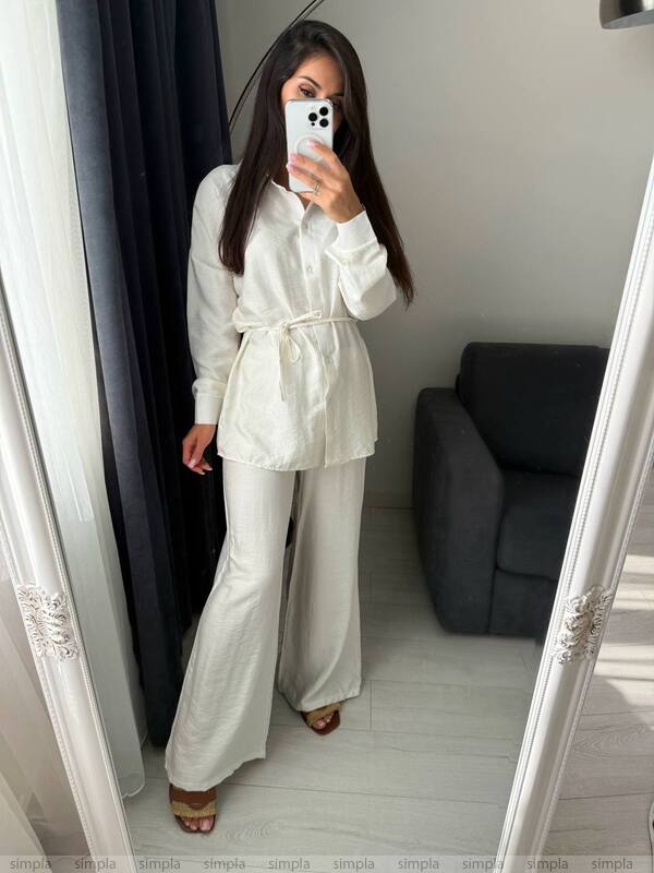 Person wearing a white outfit taking a mirror selfie in a room with a gray sofa.
