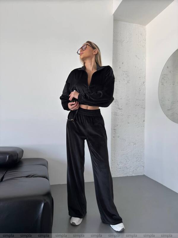 Person wearing a black outfit in a minimalistic room with a white wall and gray floor.