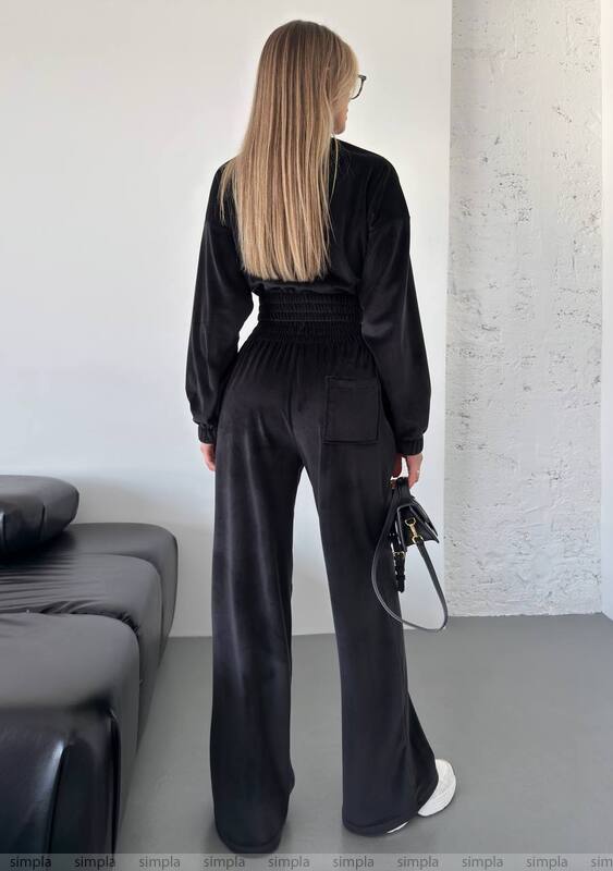 Person wearing a black outfit standing in a minimalistic room with a sofa.