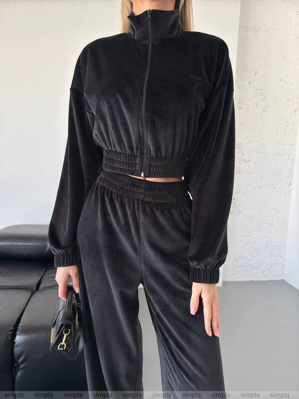 Person wearing a black tracksuit holding a black handbag indoors.
