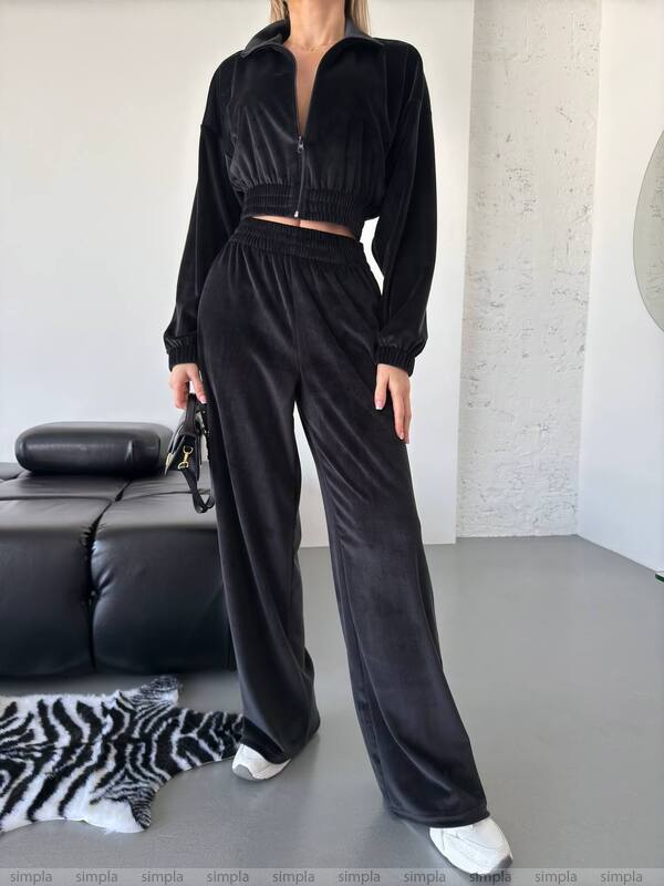 Person wearing a black tracksuit in a minimalistic room with a black sofa and zebra-patterned rug.