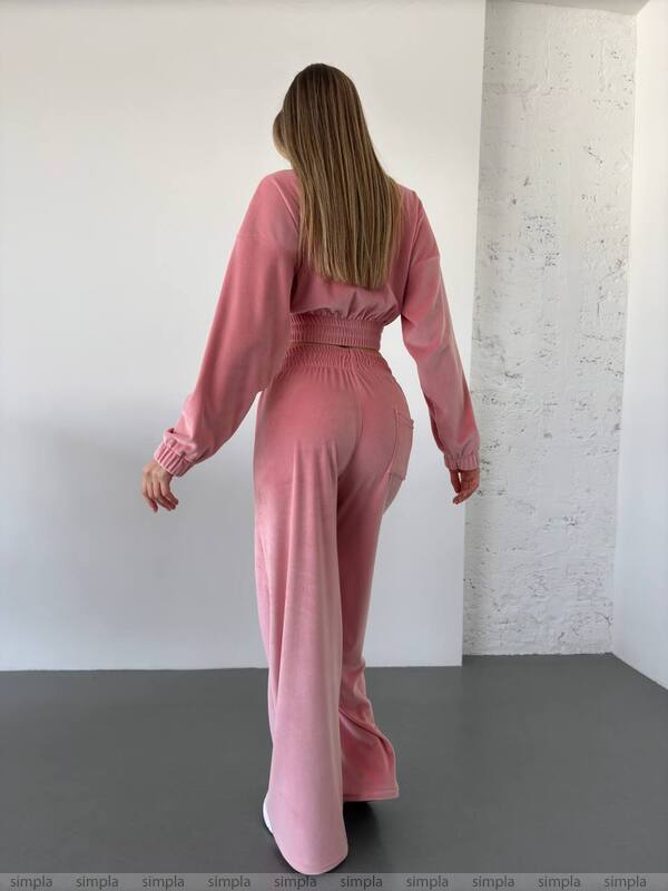 Person wearing a pink outfit standing against a white wall.