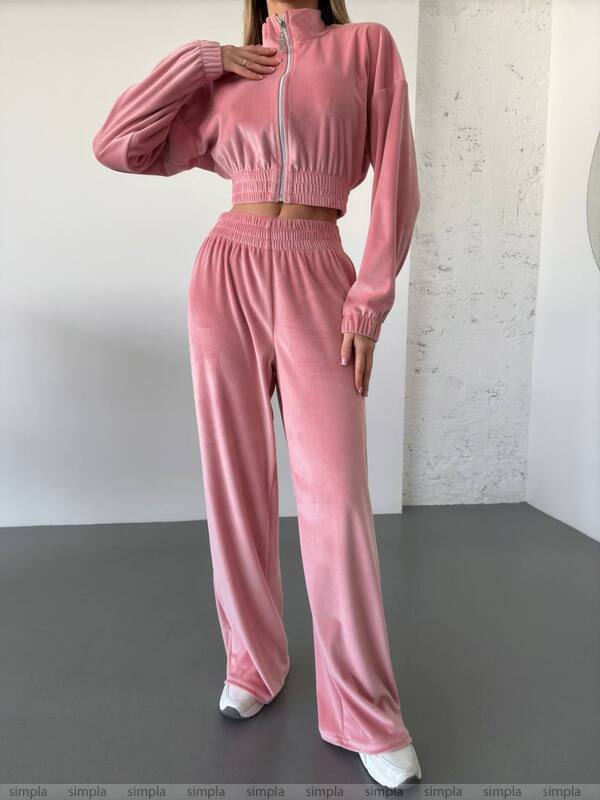 Pink tracksuit worn by a person against a white wall.