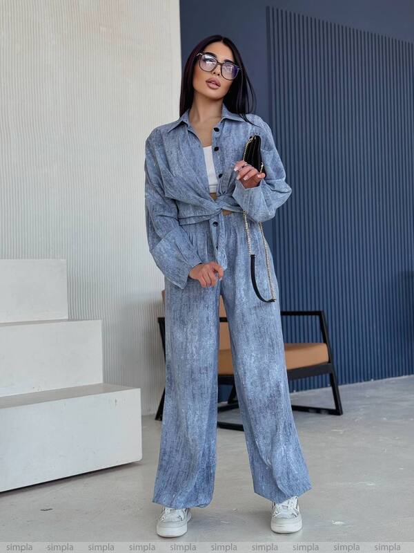 Woman in a blue denim outfit standing indoors with a phone.