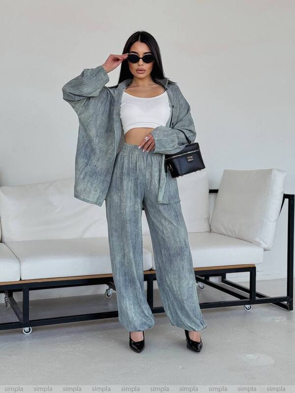 Woman in a gray outfit with a white top and wide-leg pants, standing in a minimalistic room.