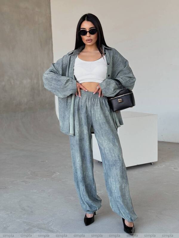 Woman in a stylish outfit with a gray jacket and pants, white top, and black sunglasses, standing against a neutral background.