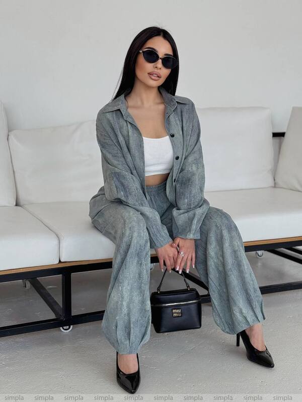 Woman in a gray outfit sitting on a white couch with a black handbag.