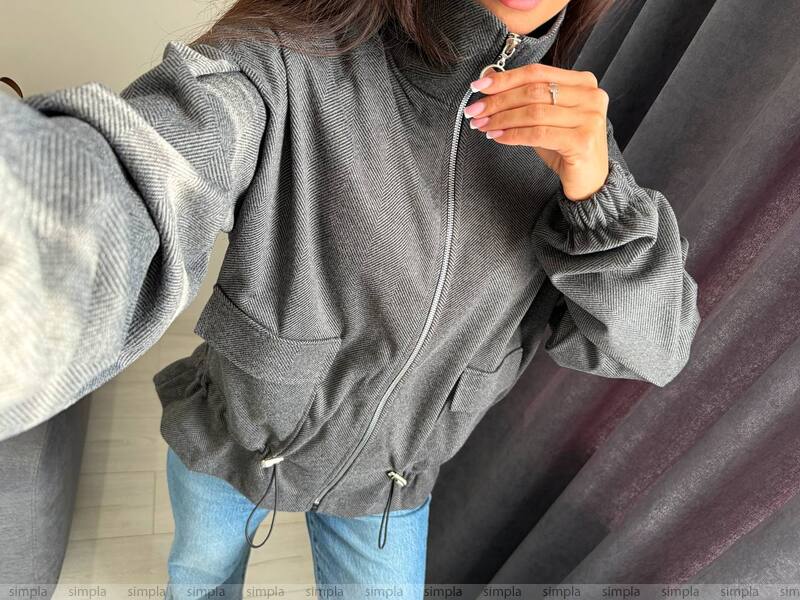 Person wearing a gray zip-up hoodie with a plain background