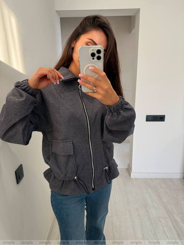 Person wearing a gray jacket taking a mirror selfie in a room.