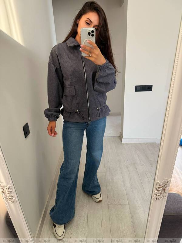 Person wearing a gray jacket and blue jeans taking a mirror selfie.