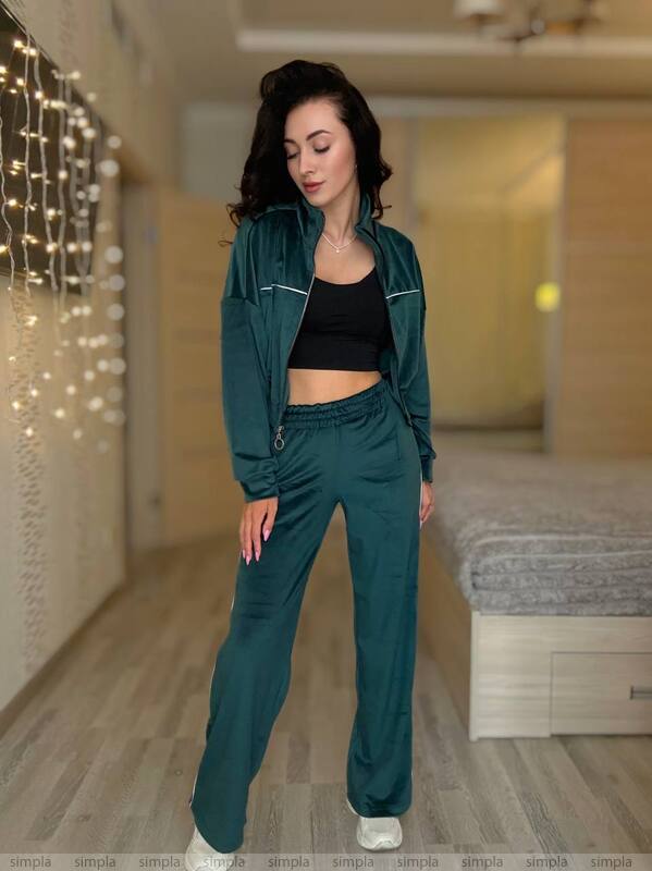 Woman wearing a teal tracksuit in a room with string lights and a bed.