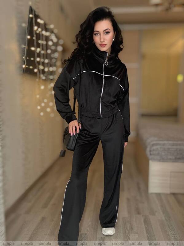 Woman in a black tracksuit standing in a room with decorative lights.