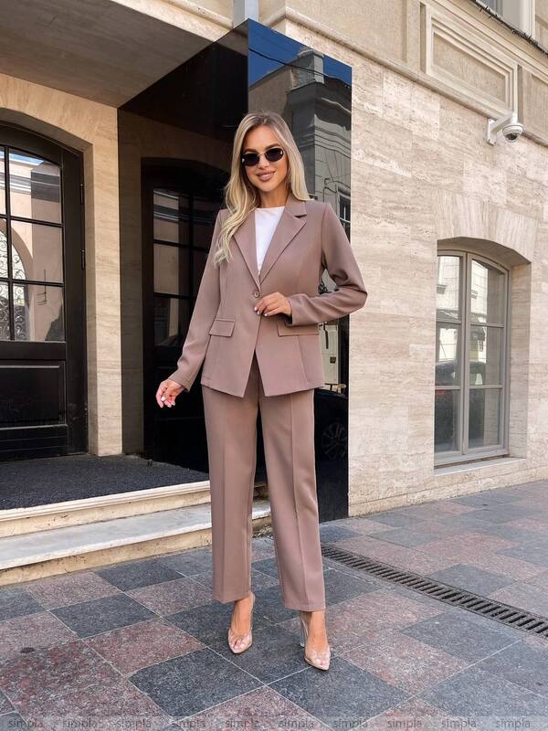 Woman in a beige suit standing in front of a building entrance.
