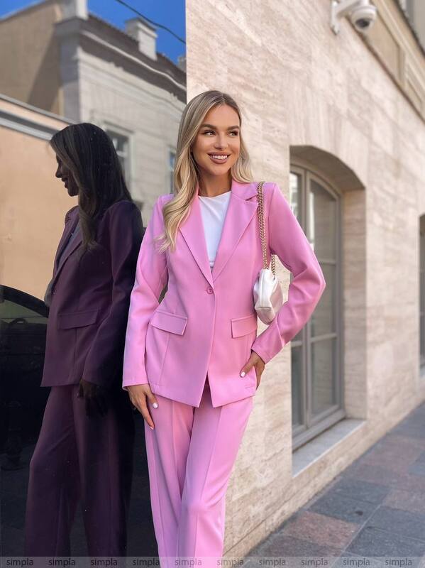 Woman in a pink suit standing against a building with another person in the background.