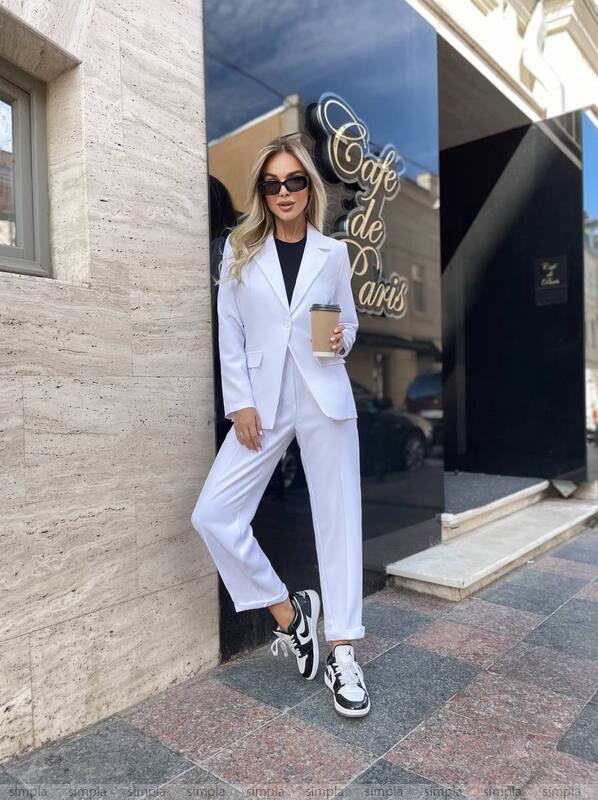 Woman in a white suit standing outside a cafe holding a coffee cup.