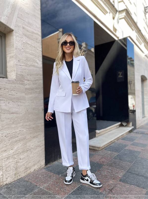 Woman in a white suit standing outside a building holding a coffee cup.