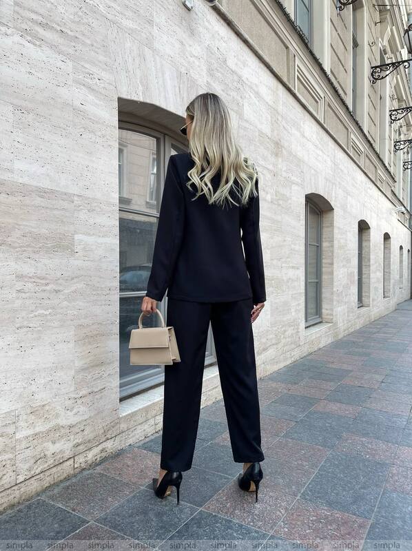 Woman in a black suit standing on a city street.