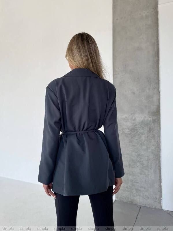 Person wearing a dark gray coat standing against a plain wall.