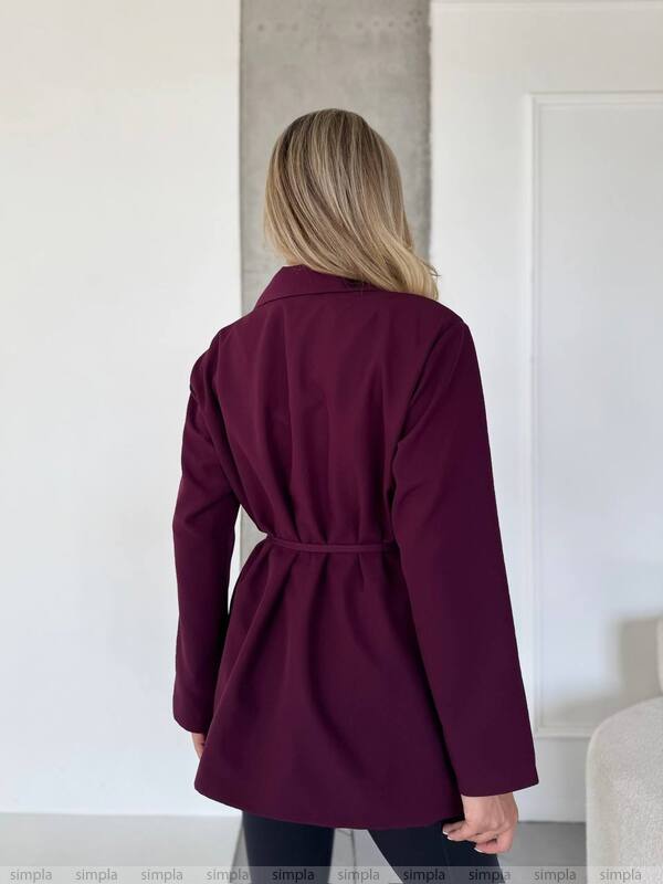 Person wearing a purple coat standing in a minimalistic room.