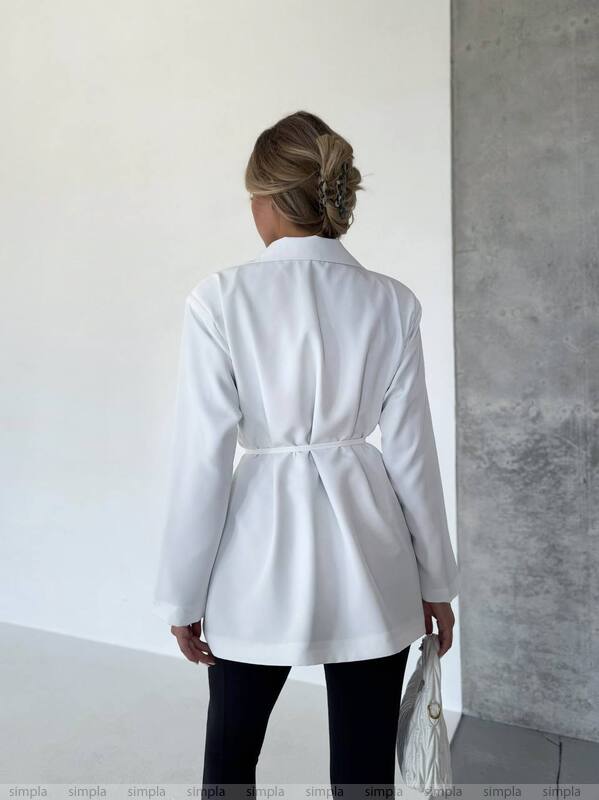 Person wearing a white coat standing against a plain wall.