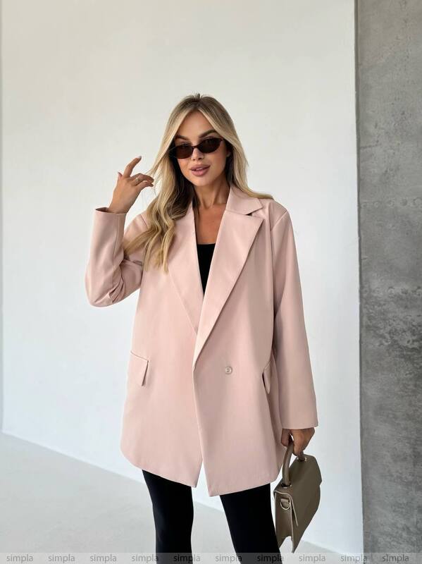 Woman wearing a pink coat with sunglasses and a handbag indoors.