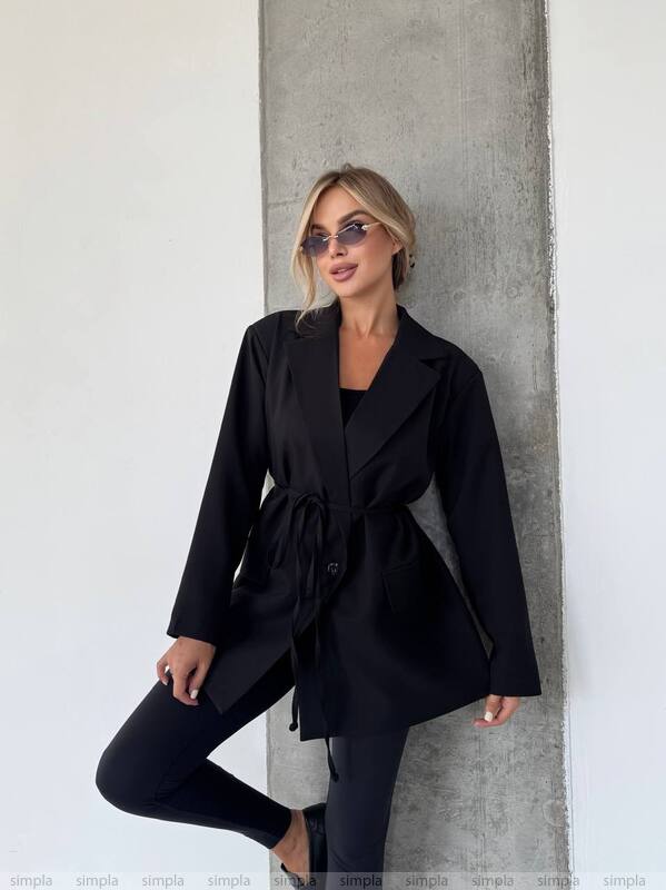 Woman wearing a black coat leaning against a concrete wall.