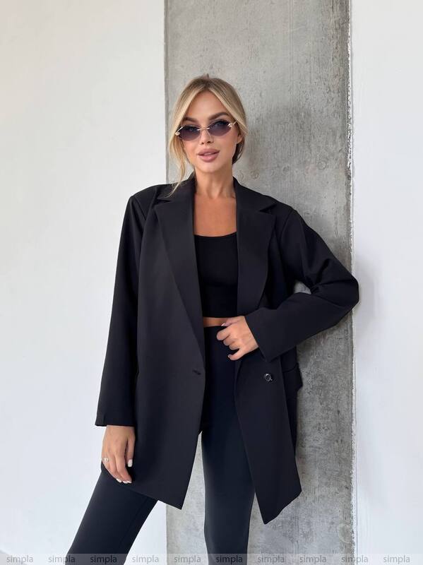 Woman wearing a black coat and sunglasses against a concrete wall.