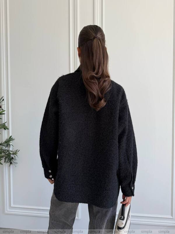 Person wearing a black coat standing in front of a white door.