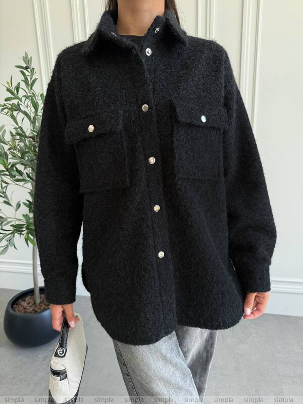 Person wearing a black jacket with button details against a neutral background