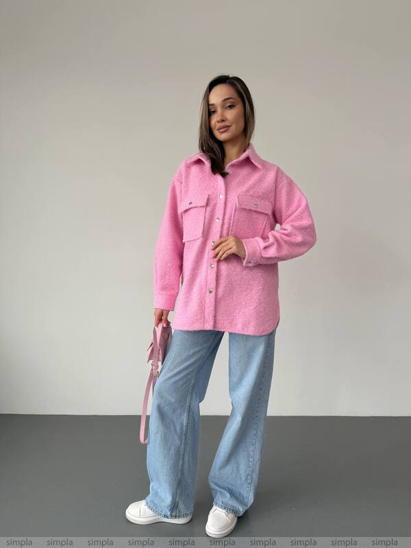 Woman wearing a pink shirt and blue jeans against a plain background
