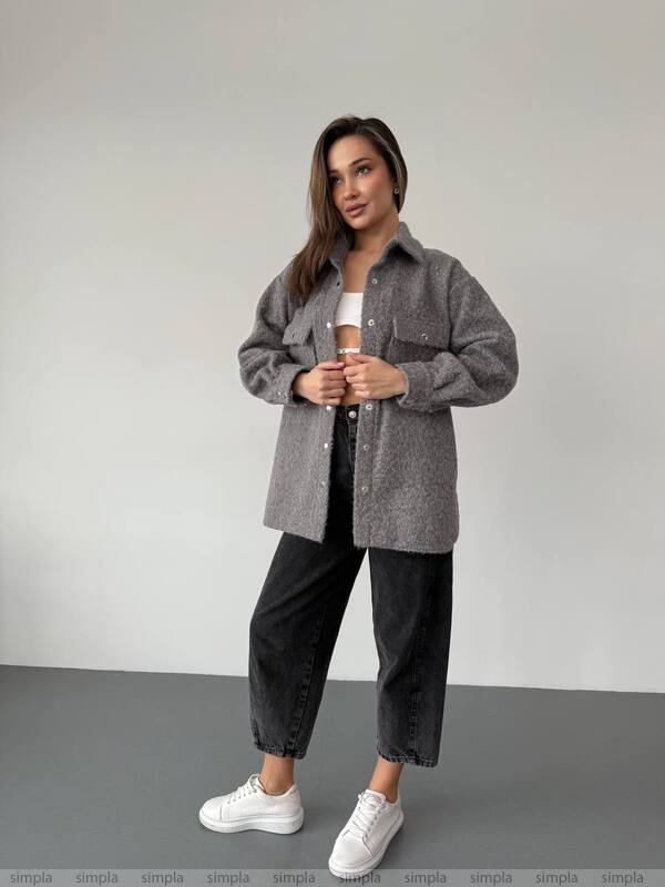 Woman wearing a gray oversized shirt, black pants, and white sneakers on a plain background