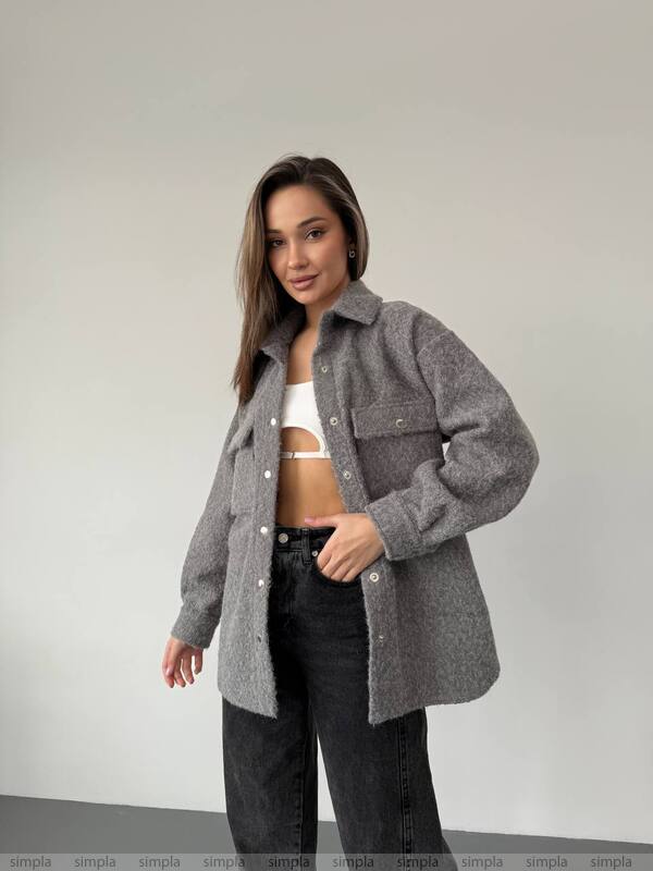 Woman wearing a gray jacket over a white top and black pants on a plain background
