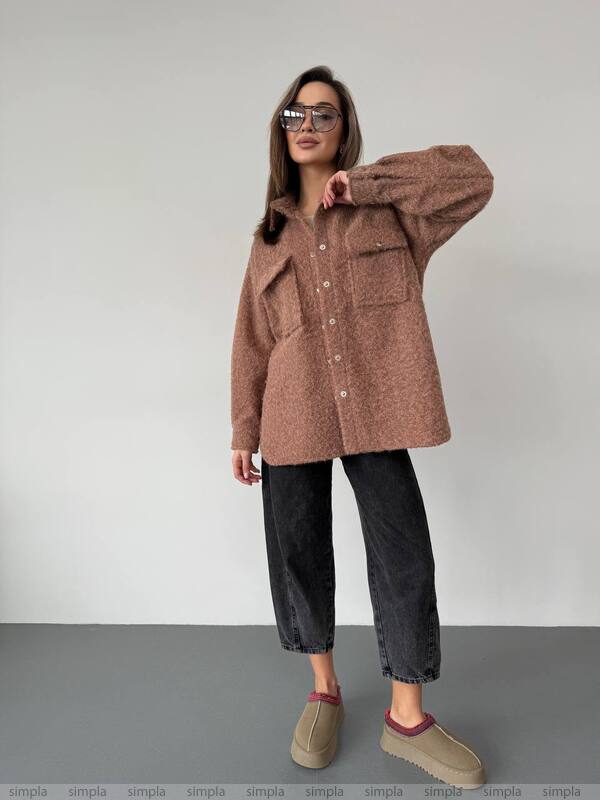 Woman wearing a brown coat and black pants against a plain background