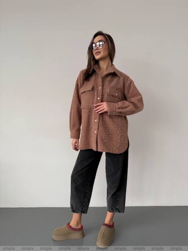 Woman wearing a brown oversized shirt and black pants against a plain background