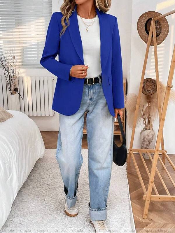 Person wearing a blue blazer, white shirt, and light blue jeans in a bedroom setting.