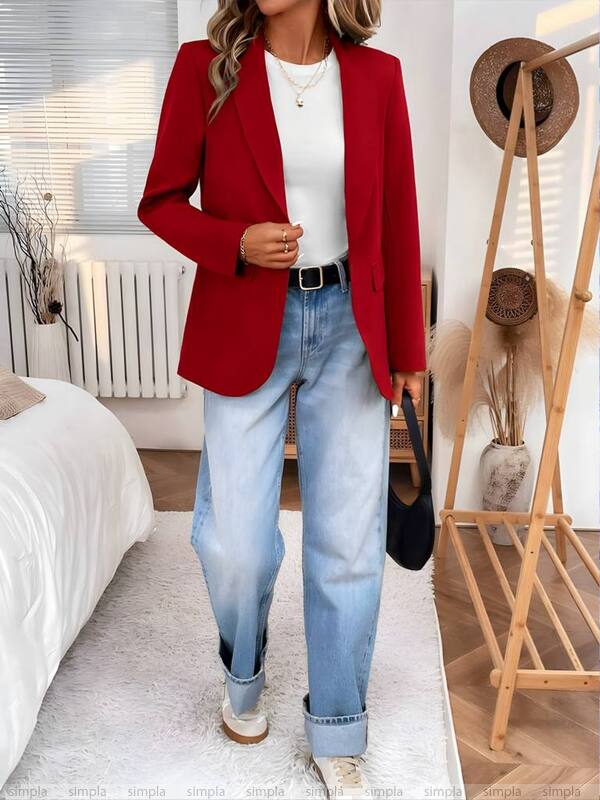 Person wearing a red blazer, white top, and blue jeans in a bedroom setting.