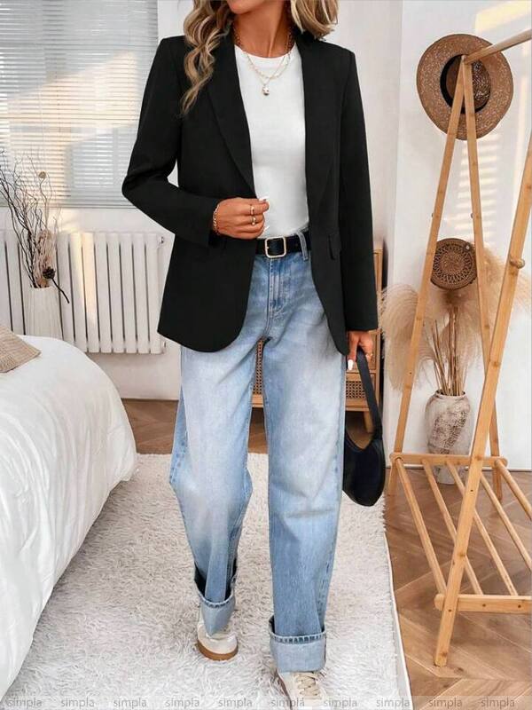 Person wearing a black blazer, white top, and blue jeans in a bedroom setting.