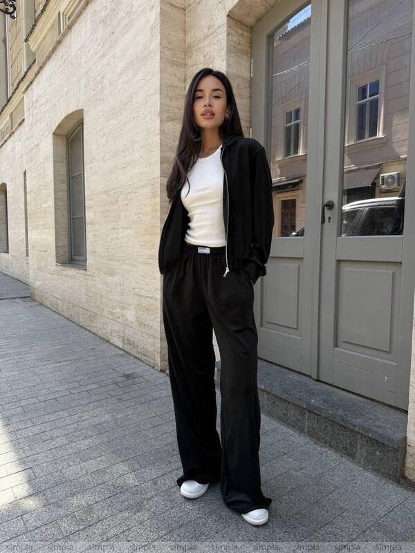 Woman in black outfit standing on a sidewalk with a building in the background