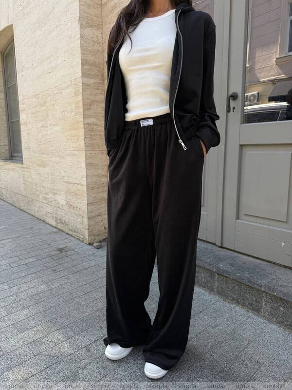 Person wearing a black outfit with a white shirt, standing on a sidewalk.