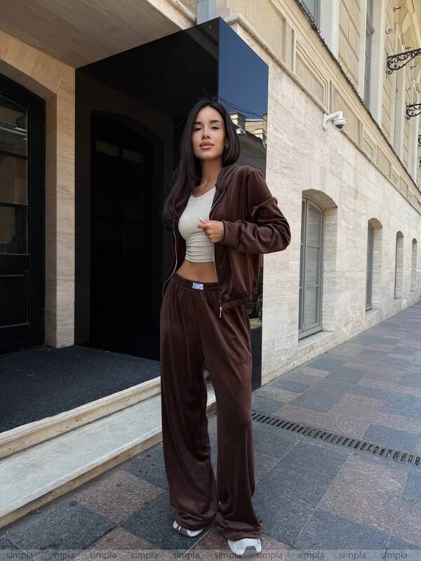Woman in a brown tracksuit standing on a sidewalk with a building in the background