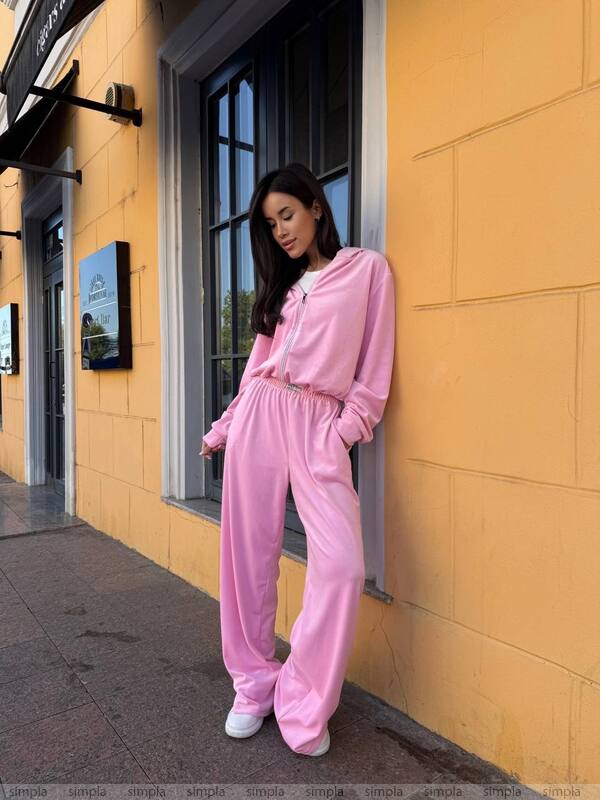 Woman in a pink tracksuit standing against a yellow wall.