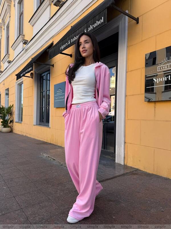 Woman in pink tracksuit standing in front of a yellow building with store signs.