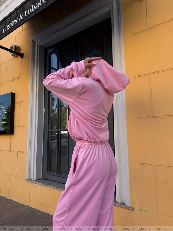 Person wearing a pink tracksuit standing in front of a yellow building with a glass door.